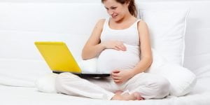 Mulher grávida deitada na cama navegando na internet