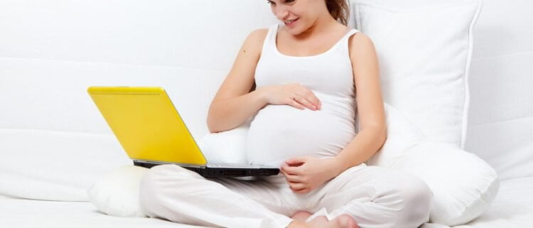 Mulher grávida deitada na cama navegando na internet